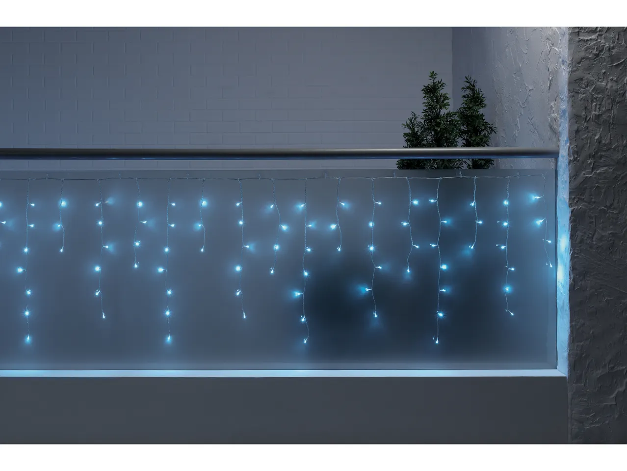 Luci di Natale a cascata blu su un balcone con ringhiera e piante.