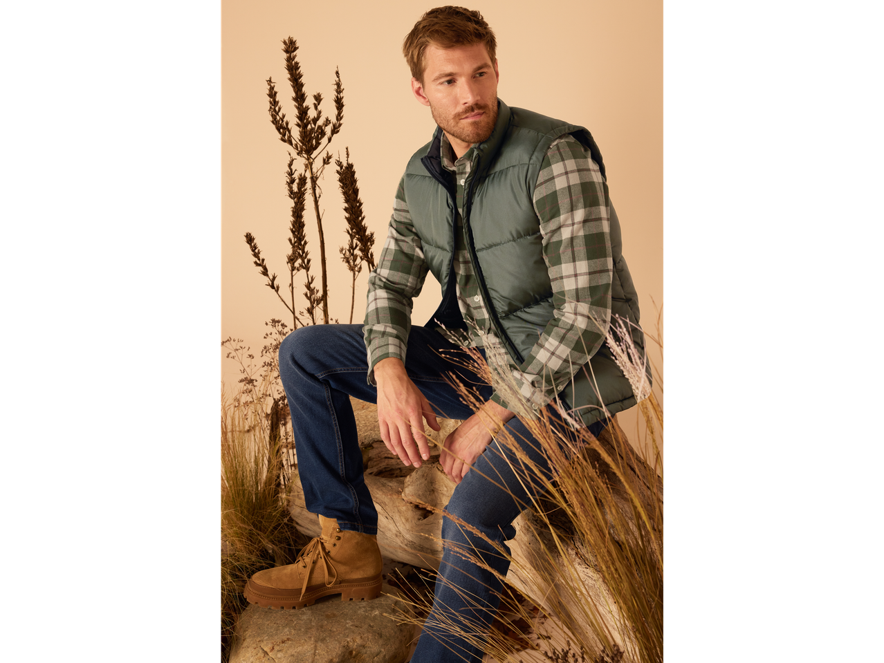 Man in flannel shirt and vest, sitting on a tree trunk.
