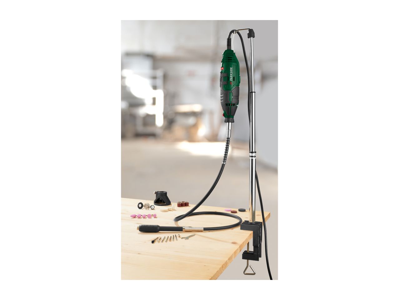 Rotary tool with flexible shaft, stand, and various accessories on a wooden table.
