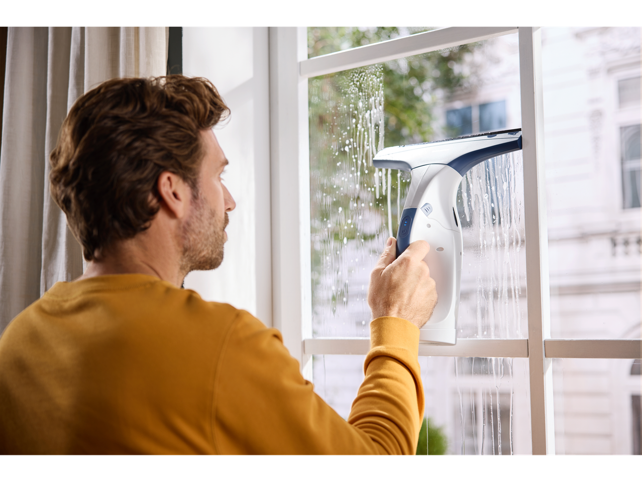 Homem a limpar uma janela com o limpa-vidros sem fios SILVERCREST, deixando espuma.