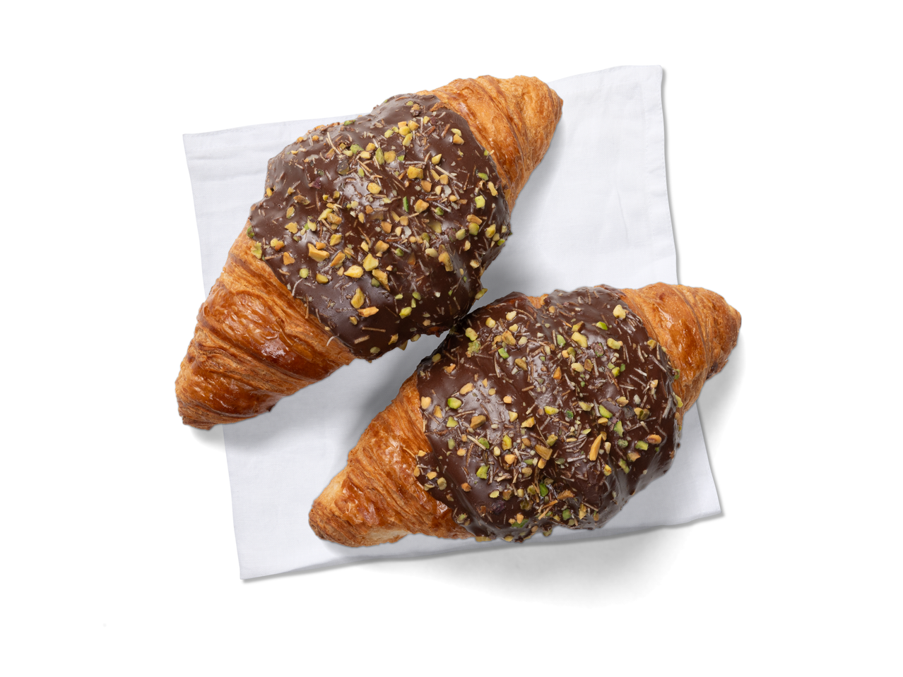 Két Dubai stílusú croissant csokoládé- és pisztáciaöntettel, fehér szalvétán.