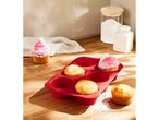A red silicone muffin pan with baked muffins, one decorated with pink frosting and coconut flakes.