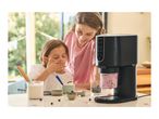 Mother and daughter making ice cream with a black ice cream maker, surrounded by blueberries and marshmallows.