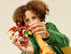 A child holding a red and yellow toy dragon, wearing a green jacket.