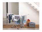White clothes drying rack with various clothes, next to a grey laundry basket and red candles.