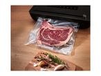 A vacuum sealer packaging a raw steak on a wooden table next to fresh herbs and garlic.