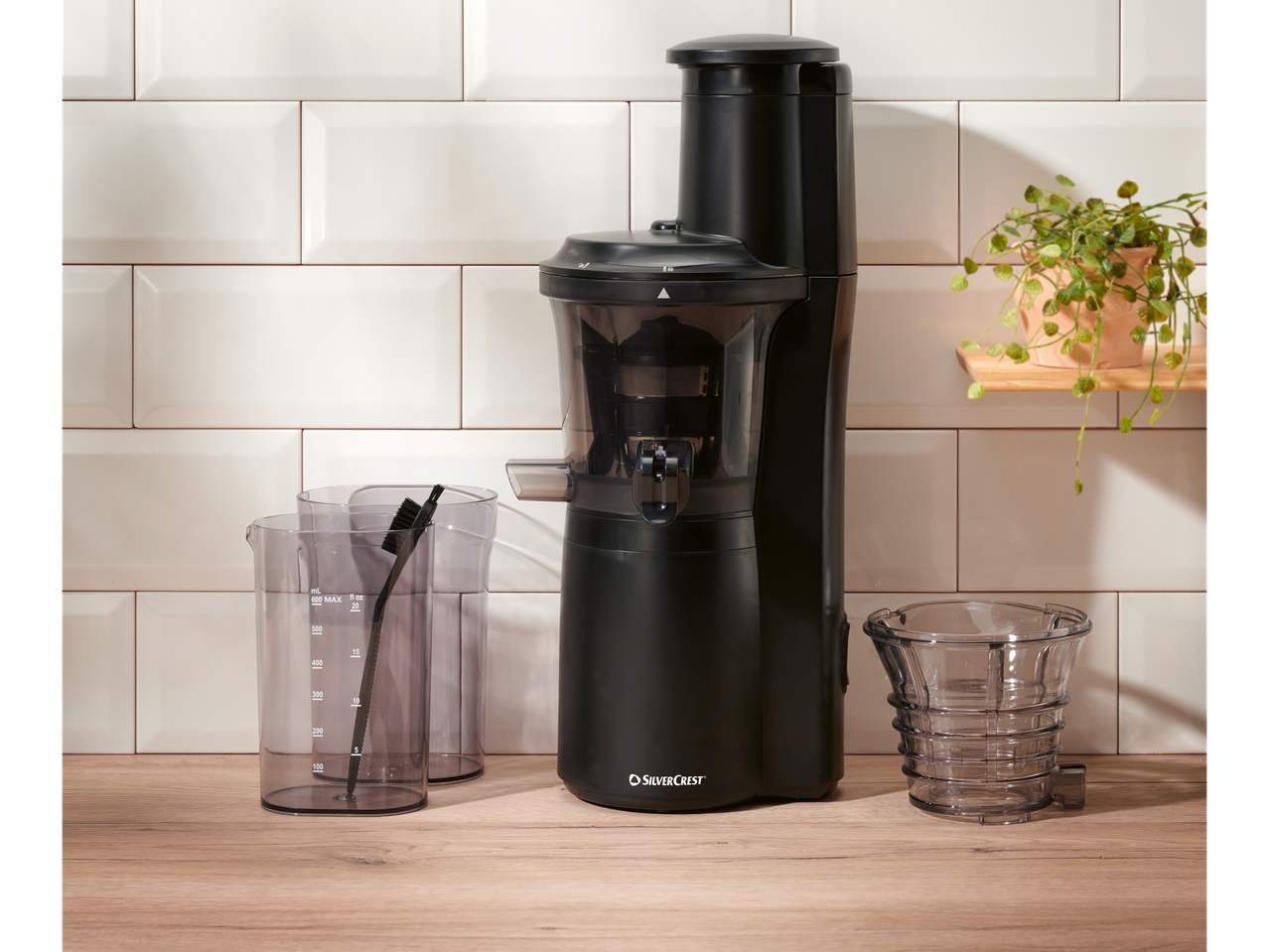 Silvercrest® slow juicer with measuring cups and cleaning brush on a wooden countertop.