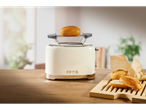 Cream-colored toaster with a bun on top, next to a cutting board with bread rolls.