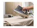 A person ironing a light-colored garment with a steam iron on an ironing board.