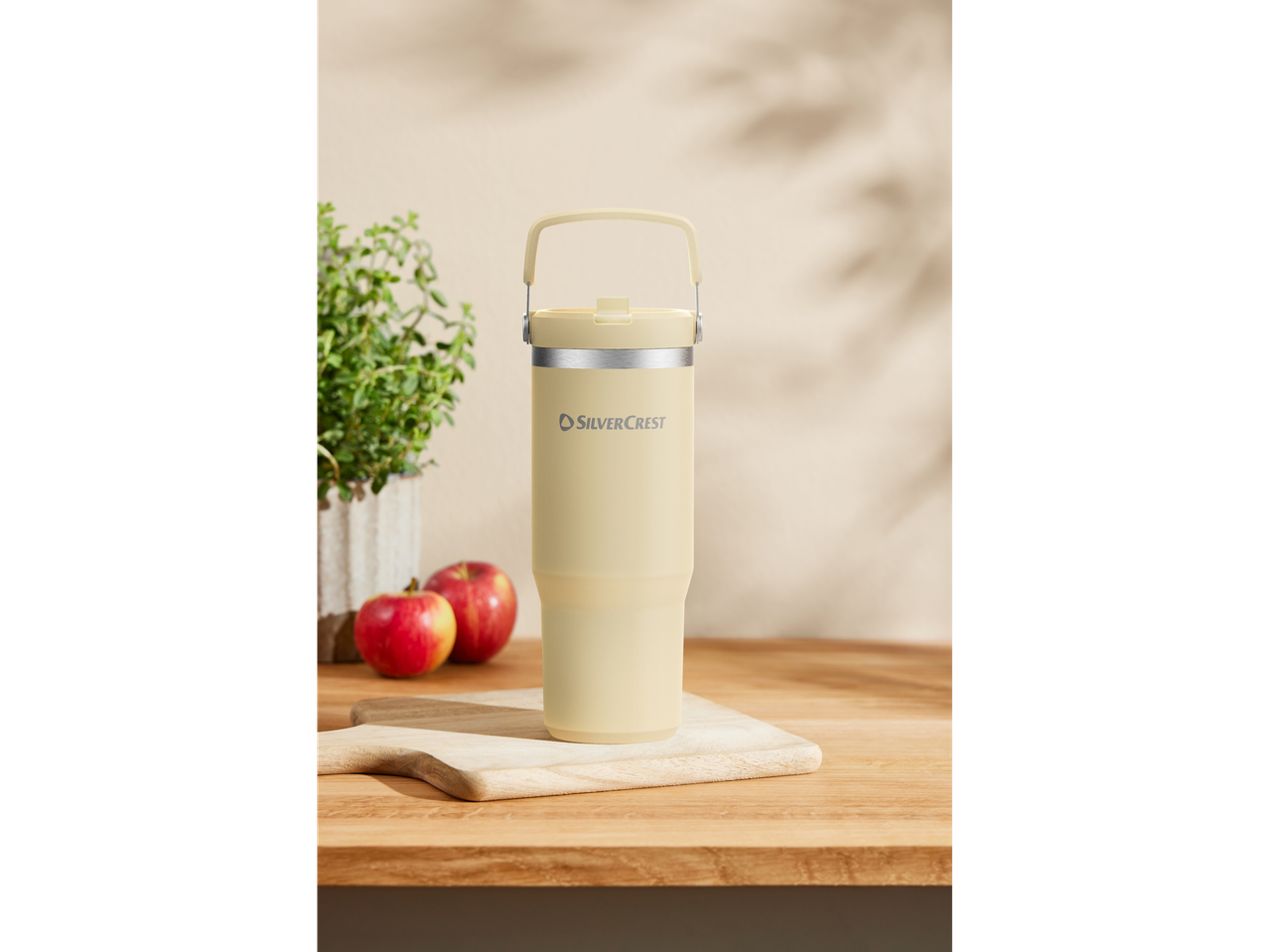 A SilverCrest pastel yellow thermos with a carrying handle sits on a wooden cutting board.