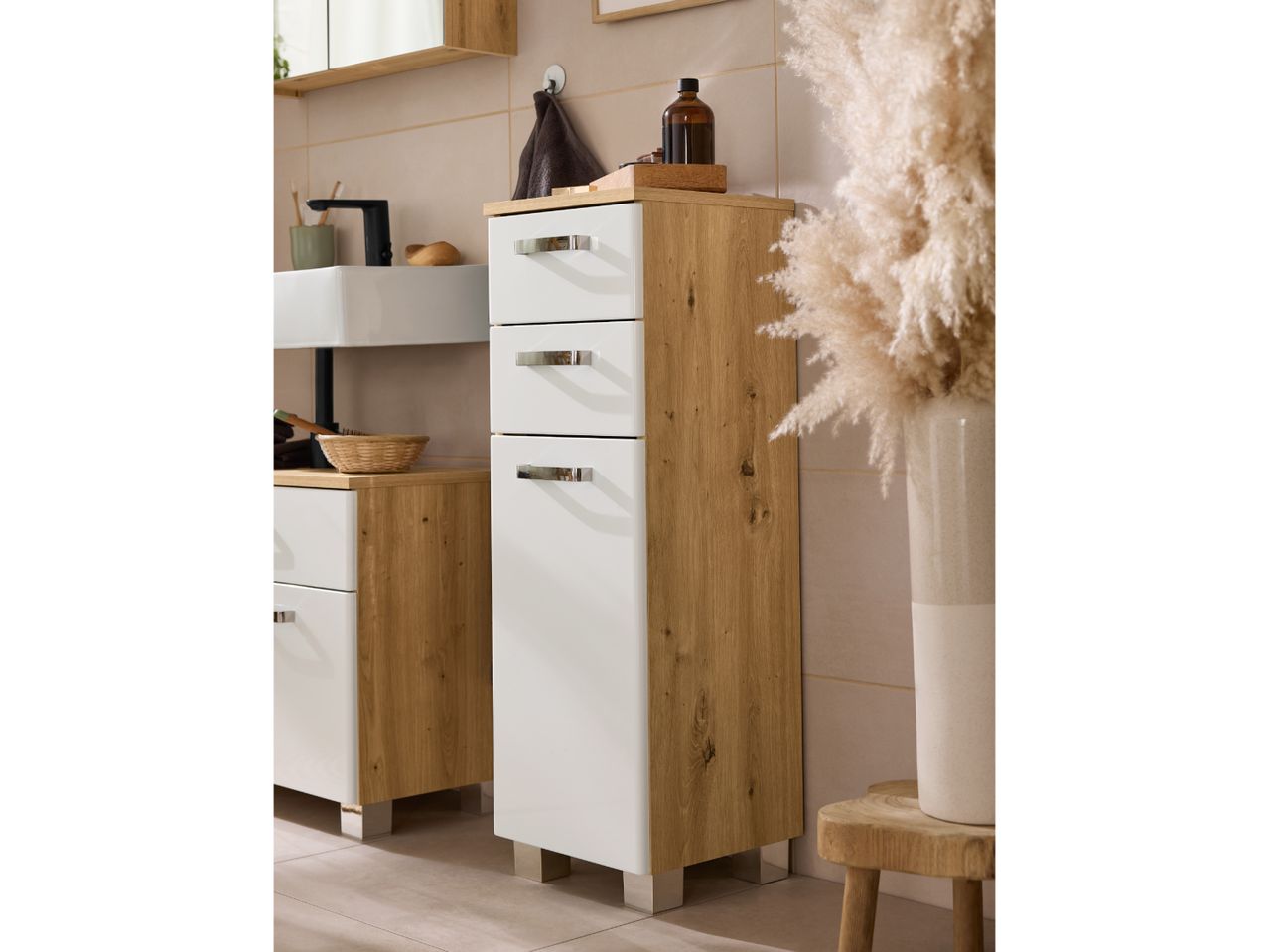 Bathroom furniture set with white and wood-effect cabinets, sink, and decorative pampas grass.