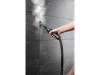 Uma pessoa limpa azulejos escuros de cerâmica com um limpador a vapor.
