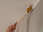 A hand holds a paintbrush applying white paint to a corner.