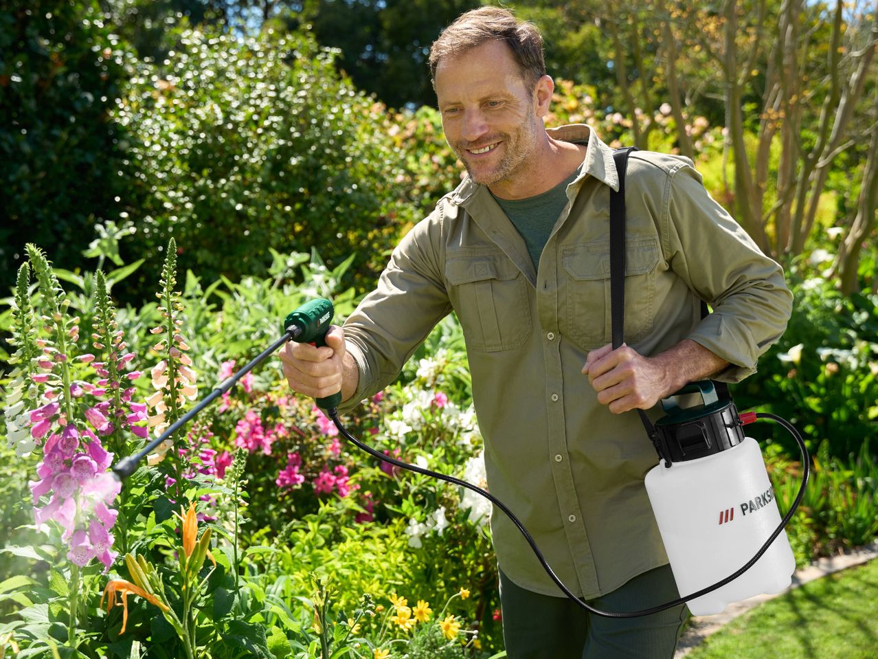 Man spraying plants in a garden with a garden sprayer.