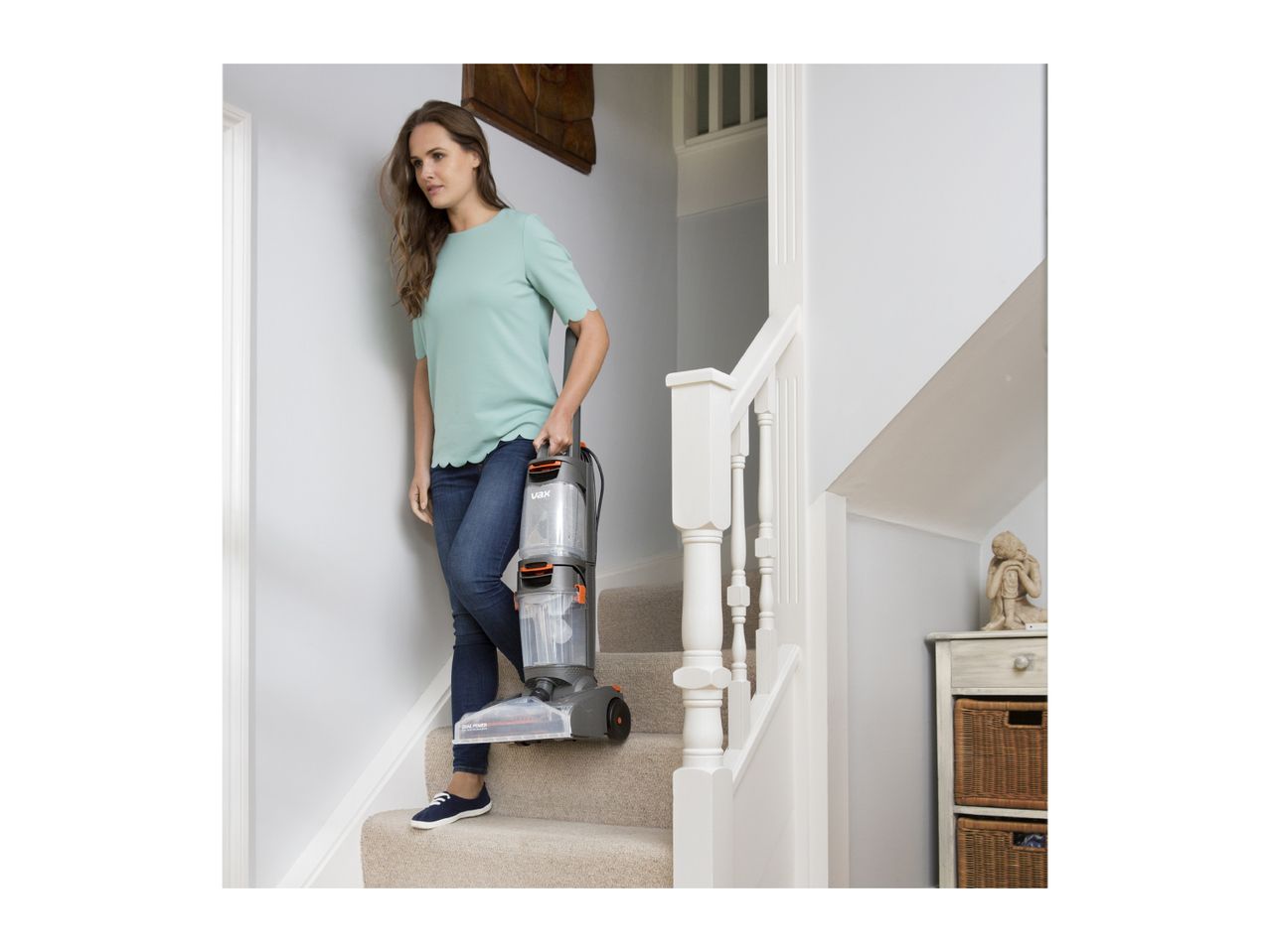 Woman carrying a Vax carpet cleaner down carpeted stairs.