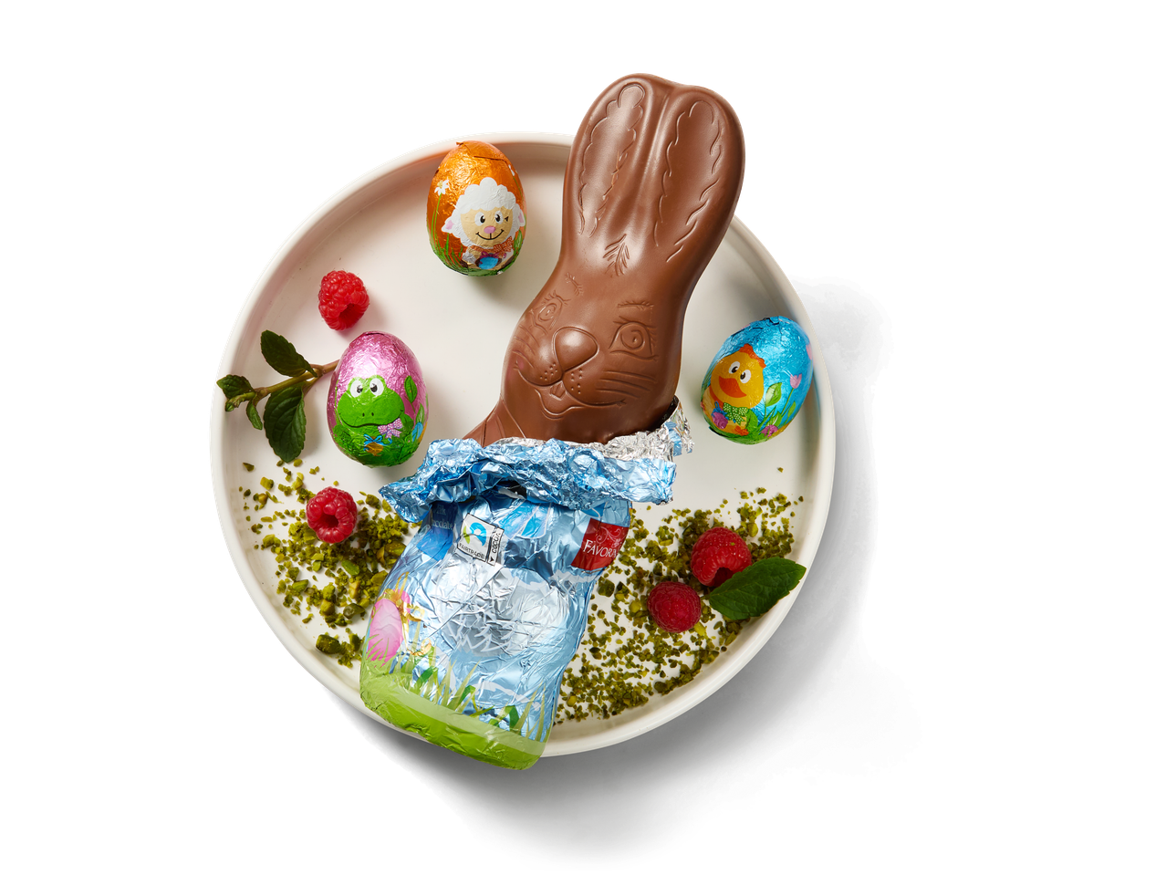 Chocolate Easter bunny and foil-wrapped eggs on a white plate with raspberries and pistachios.