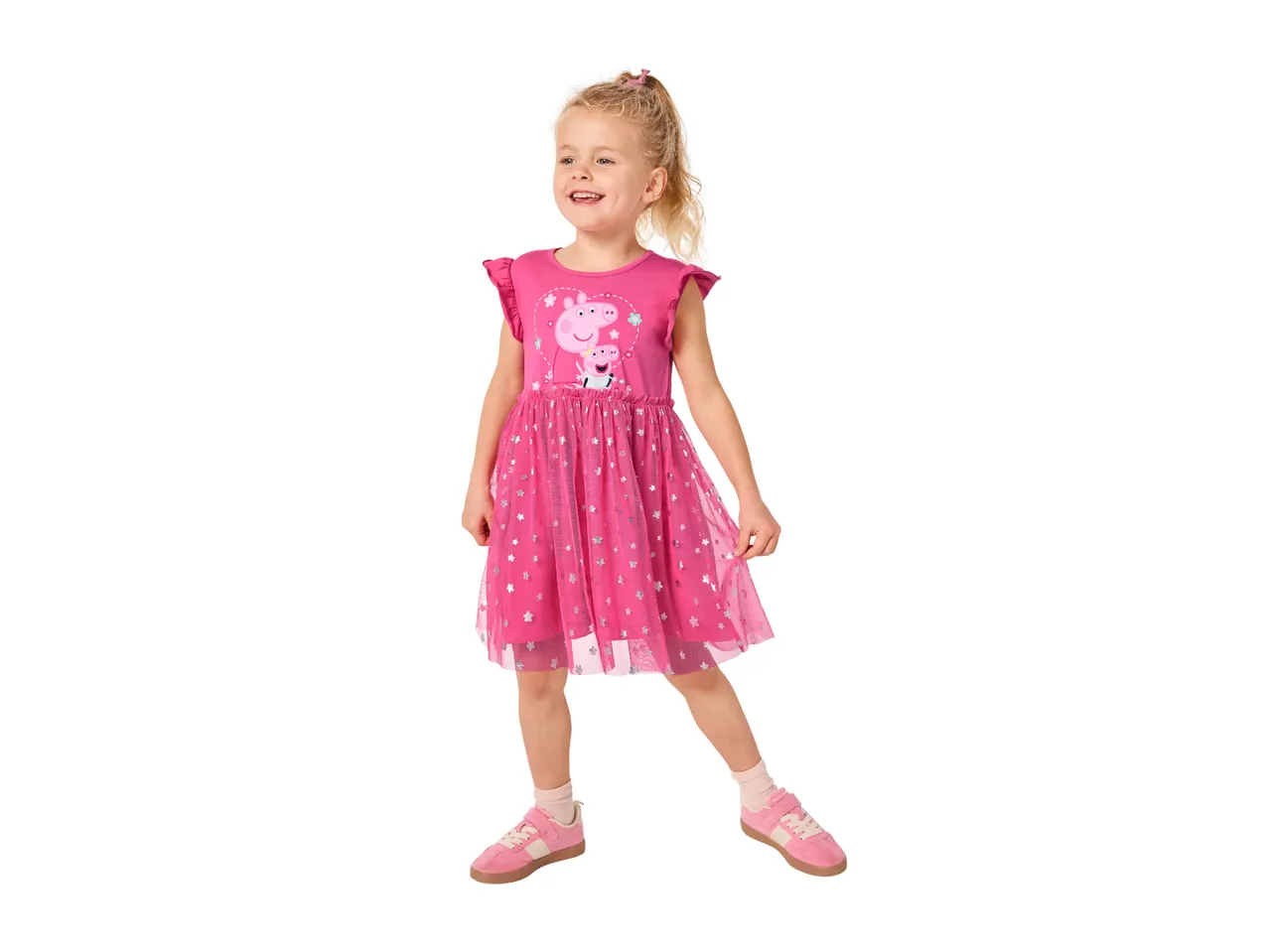 Smiling girl in a pink dress with pig characters and silver stars, wearing pink sneakers.