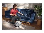 A woman cleans a blue velvet sofa with a portable spot carpet cleaner.