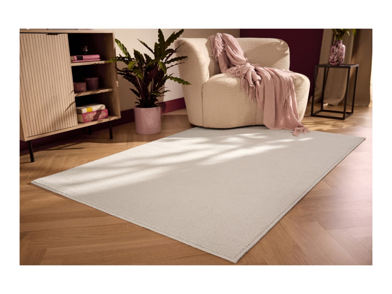 A light beige rug on a wooden floor in a living room with a cabinet, plant, and armchair.