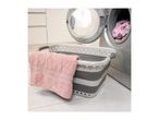 A pink towel rests on a grey and white collapsible laundry basket next to a washing machine.