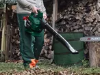 Person holding a leaf blower, with a chainsaw and stacked firewood in the background.