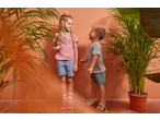Two kids in Lupilu T-shirts and shorts, surrounded by plants, smiling at each other.