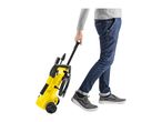 Person pulling a yellow pressure washer with black accents on wheels.