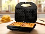 A black double waffle maker with two golden waffles cooking inside.