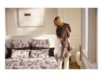 A woman styling a bed with floral patterned bedding and a brown knit throw blanket.
