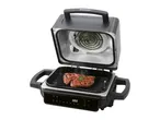 Open electric grill with two steaks cooking on the grates, showing the heating element.