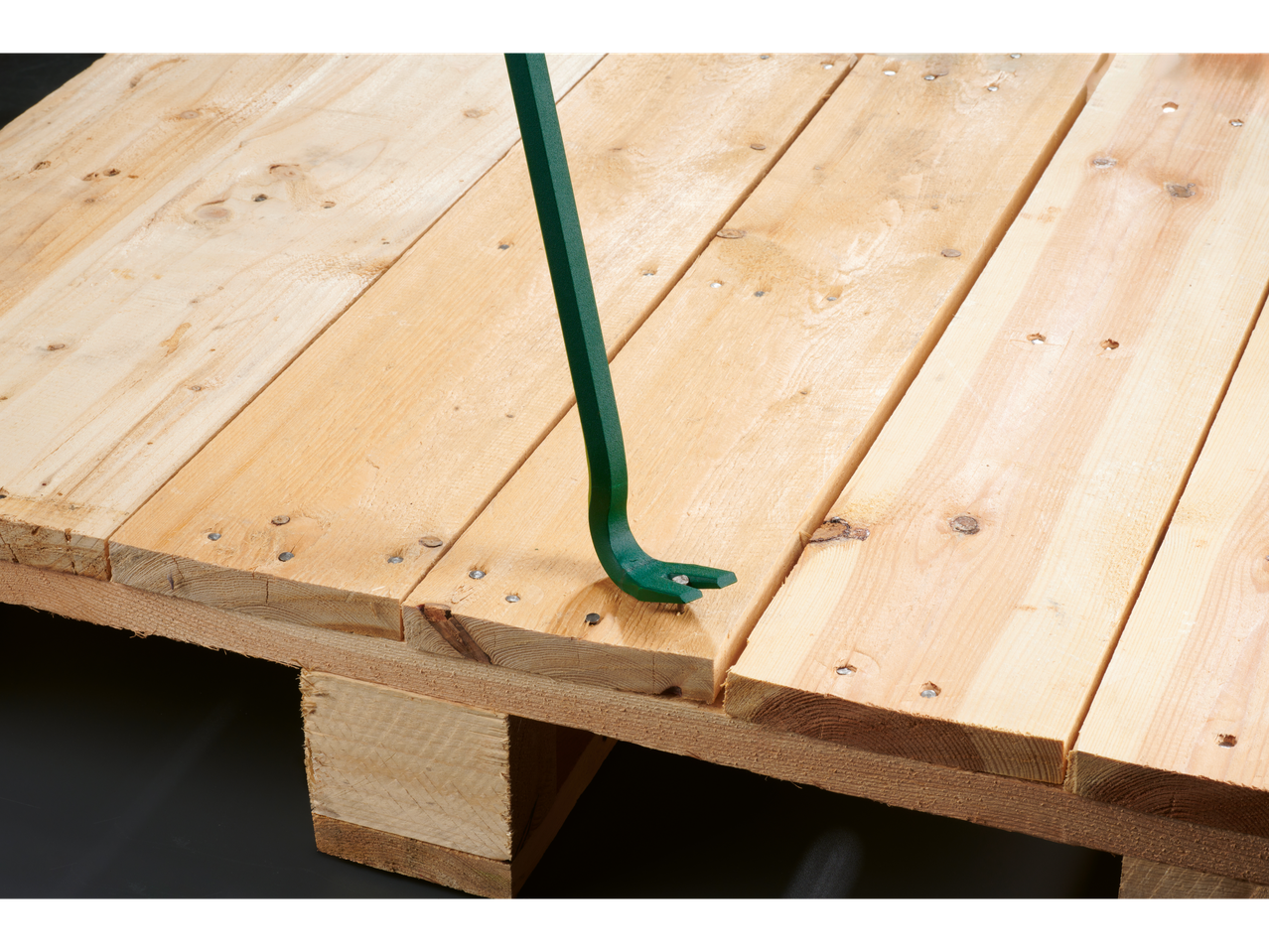 A green crowbar is used to pry apart two wooden planks on a pallet.