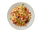 Pasta with tomato sauce, zucchini, capers, and basil on a striped plate.