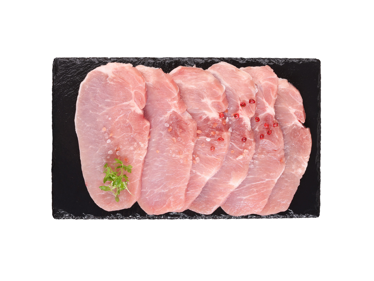 Sveži svinjski kotleti sa začinima i začinskim biljem na crnoj ploči.