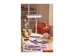 A white desk lamp illuminates a wooden desk with craft supplies and papers.