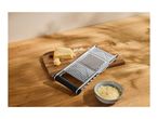 Cheese grater with a block of cheese and a bowl of grated cheese on a wooden board.