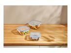 Three glass food storage containers with blue lids on a wooden counter.