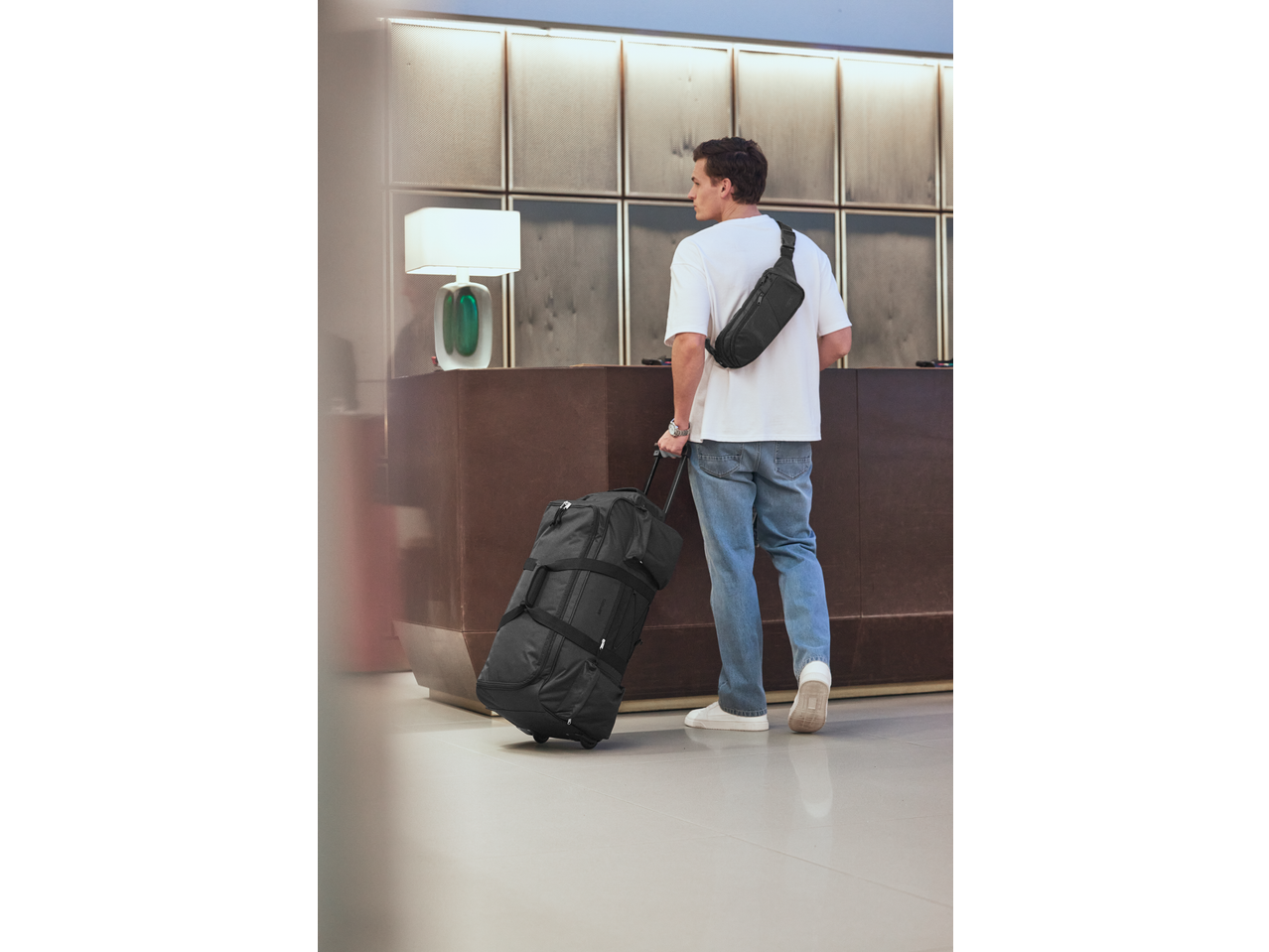 Man with a black duffel bag and a black crossbody bag at a hotel reception.