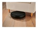 Robot vacuum cleaner under a beige armchair on a wooden floor.