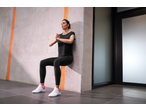 Mulher de leggings e t-shirt pretas, e sapatilhas CRIVIT brancas, a fazer agachamento na parede.