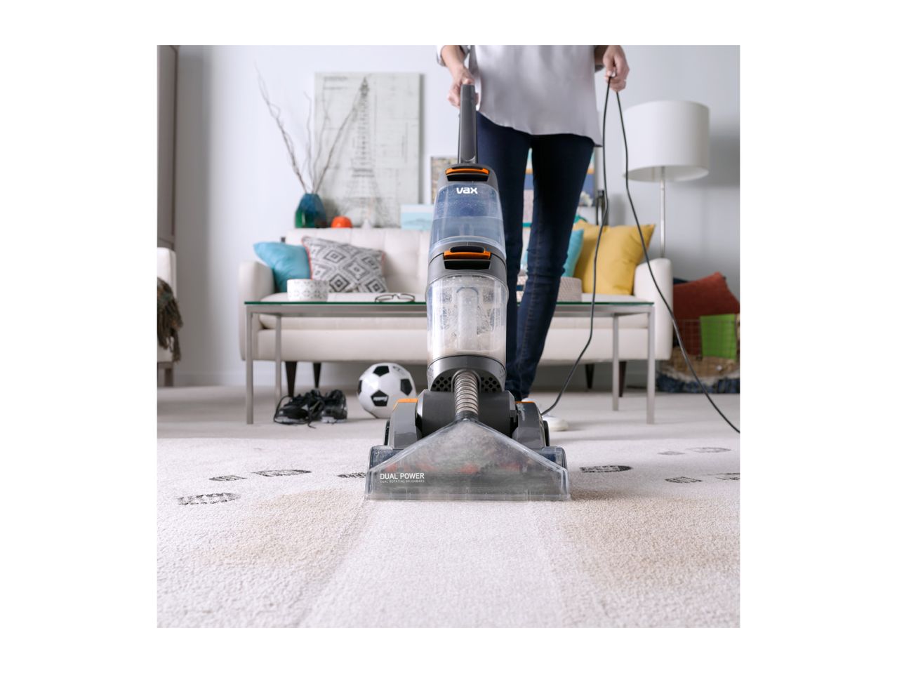 A person cleaning a dirty carpet with a Vax carpet cleaner in a living room.