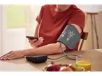 Person measuring blood pressure with SENSIPLAST® blood pressure monitor and using a smartphone.
