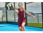 Vrouw in bordeauxrode jurk speelt padel met CRIVIT racket en bal op blauwe baan.