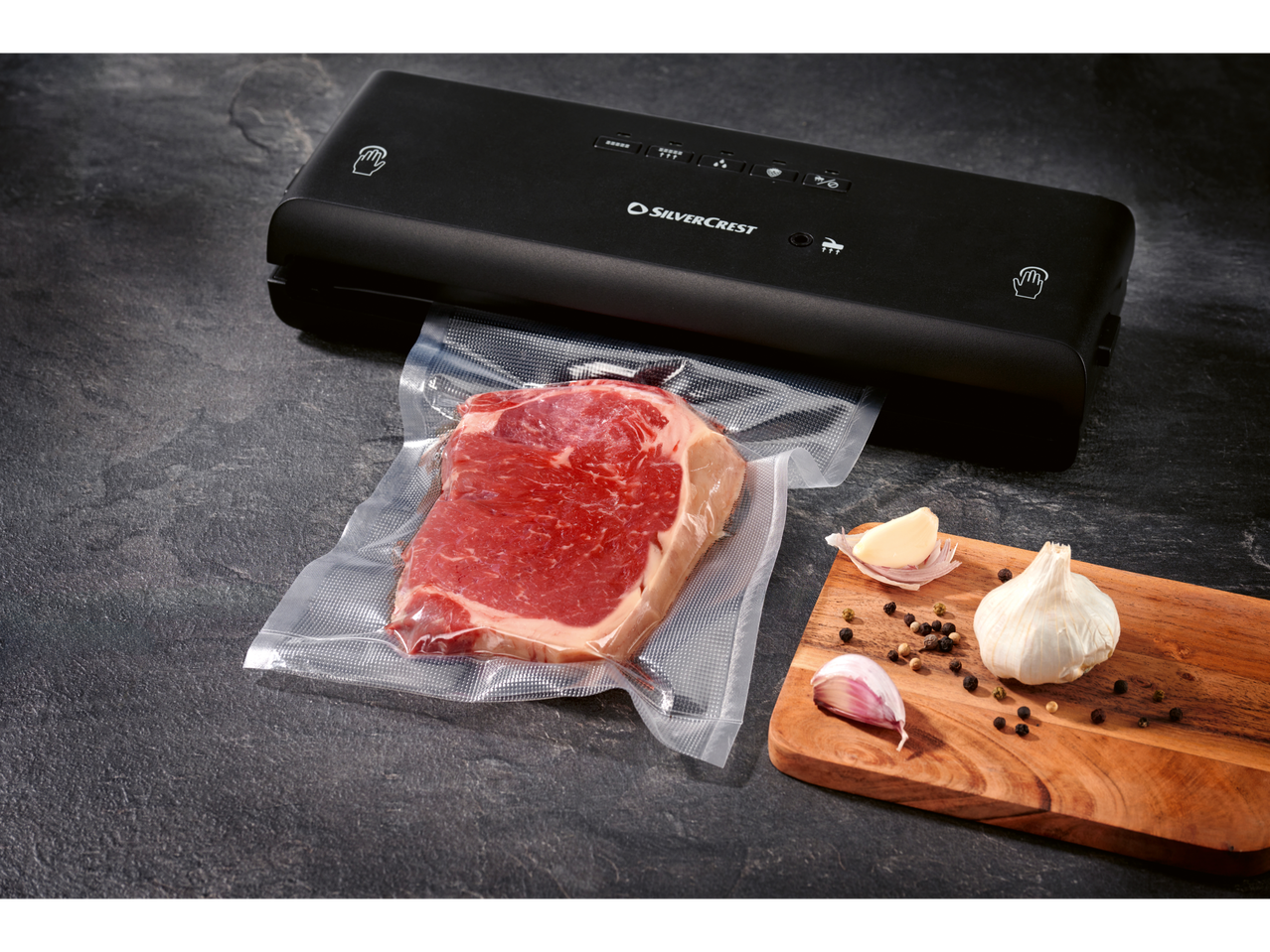 SILVERCREST® vacuum sealer with meat in a vacuum sealer roll, garlic, and peppercorns.