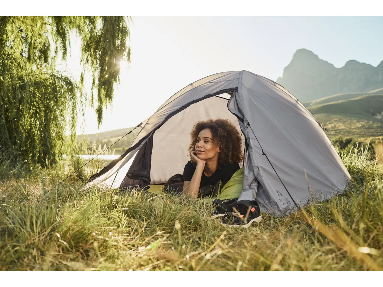 Donna rilassata dentro una tenda da campeggio in un paesaggio naturale.