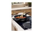 Frying pan with food and wooden spoon on an induction hob in a modern kitchen.
