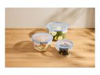 Three glass food storage containers with blue lids, filled with salad, zucchini, and olives.