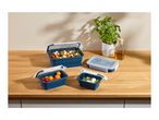 Collapsible food containers with salad, tomatoes, and mozzarella on a wooden counter.