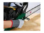 A person wearing protective gloves uses a wrench to adjust a chainsaw on a wooden table.