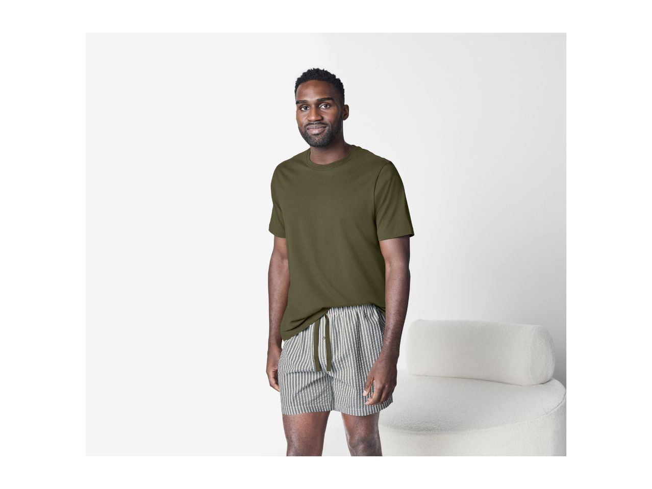 Man in a green t-shirt and striped shorts standing next to a white chair.