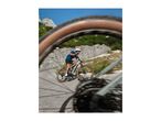 Man cycling on a mountain bike on a winding road, seen through a blurred wheel.